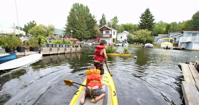 Kids paddleboarding past cottages and docks